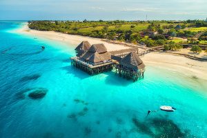 Aerial view of beautiful hotel in Indian ocean at sunset in summer. Zanzibar, Africa. Top view. Landscape with wooden hotel on the sea, azure water, sandy beach, green trees, boat. Luxury resort