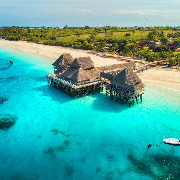 Aerial view of beautiful hotel in Indian ocean at sunset in summer. Zanzibar, Africa. Top view. Landscape with wooden hotel on the sea, azure water, sandy beach, green trees, boat. Luxury resort